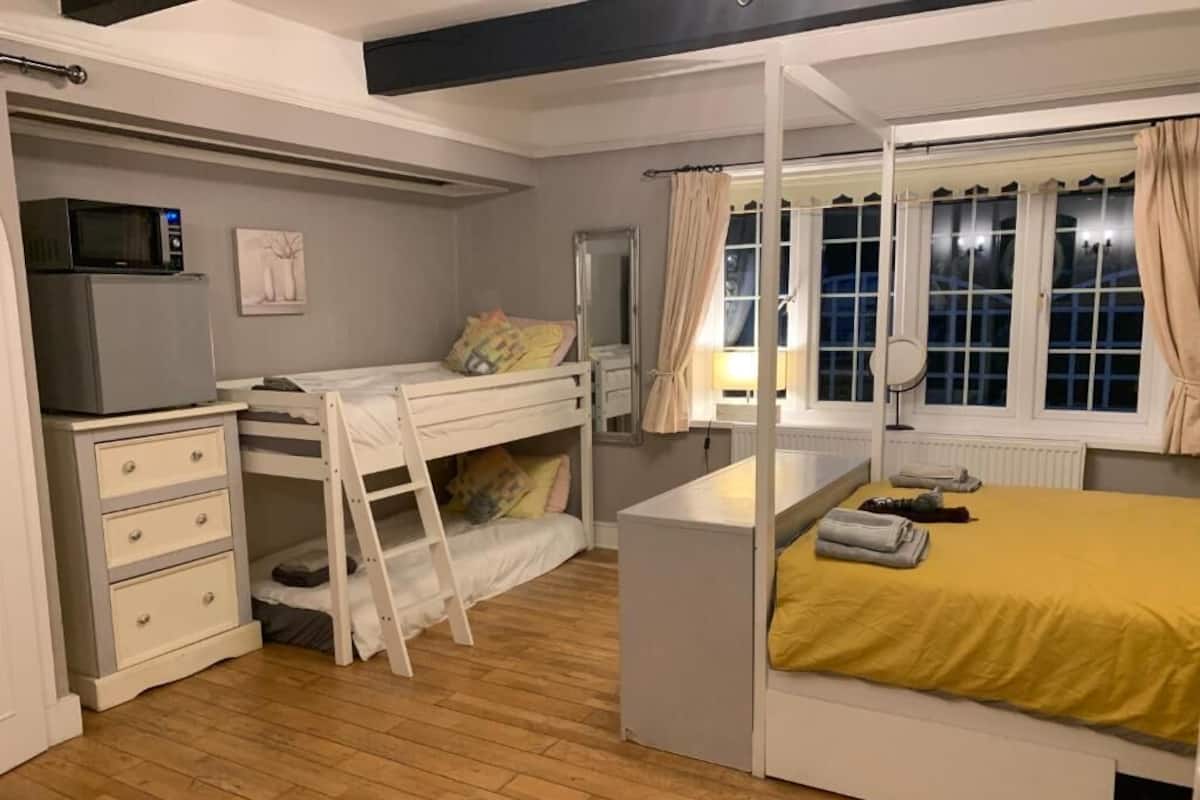 Ein Schlafzimmer mit einem Etagenbett, einem Schreibtisch mit Mikrowelle, einem Schminktisch und einem Fenster mit Vorhängen.