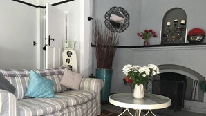 Ein Wohnzimmer mit einem gestreiften Sofa, einem runden Tisch mit Blumenvase, einem Kamin und einem Spiegel an der Wand.