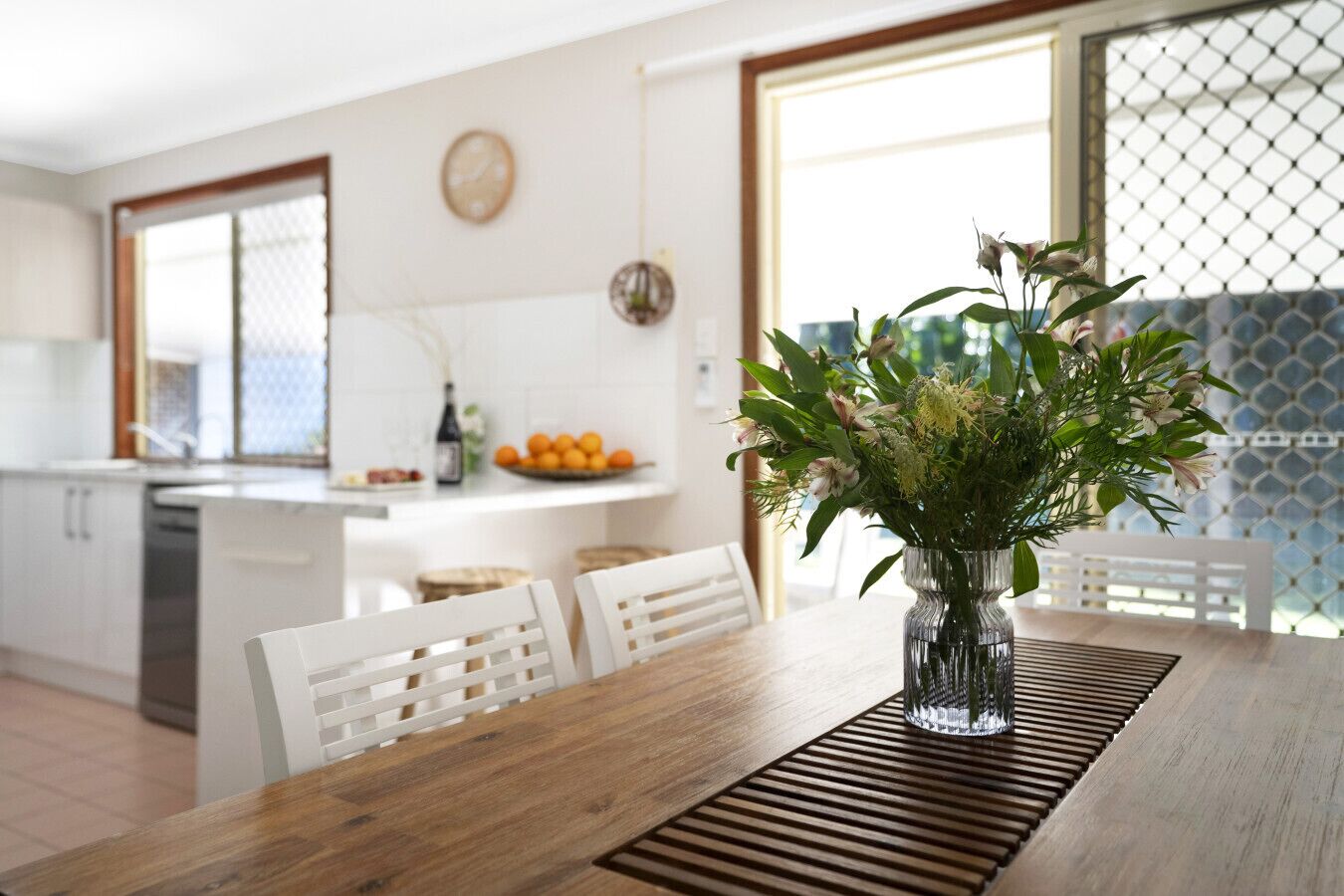 Une cuisine moderne avec des meubles blancs, une table à manger en bois et un vase rempli de fleurs.