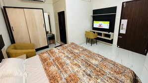 A bedroom with a bed, a wardrobe, a desk with a chair, a television, and an air conditioning unit. - COCOBAY INN (Kannur)