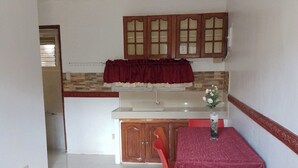 Una cocina con comedor, que presenta piso de baldosas, armarios de madera y una mesa roja con sillas a juego.