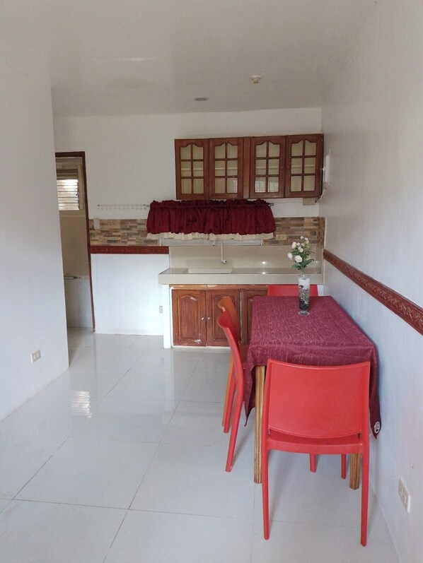 Una cocina con comedor, que presenta piso de baldosas, armarios de madera y una mesa roja con sillas a juego.