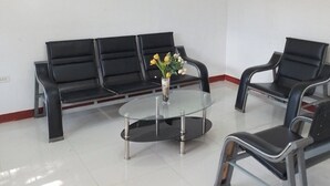 Un área de espera con un sofá negro, dos sillones y una mesa de centro de vidrio con un florero.