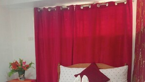 Una cama bien hecha con ropa de cama blanca y roja, un par de pantuflas blancas y una almohada decorativa.