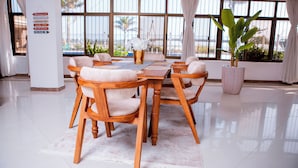 Ein Essbereich mit Holztisch und -stühlen, großen Fenstern mit Vorhängen sowie einem Blumentopf.