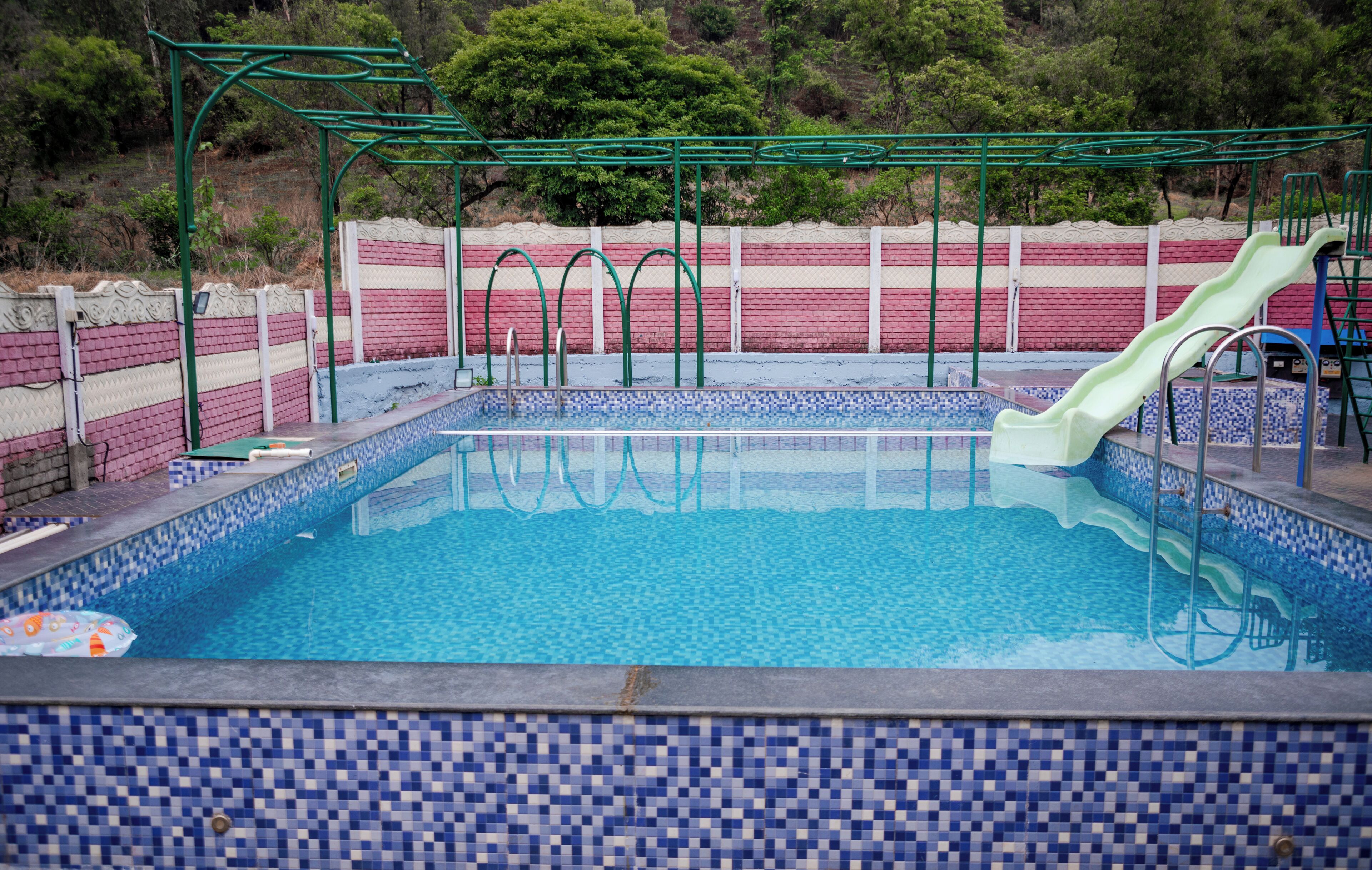 A swimming pool with a slide, surrounded by a tiled deck and a brick wall.