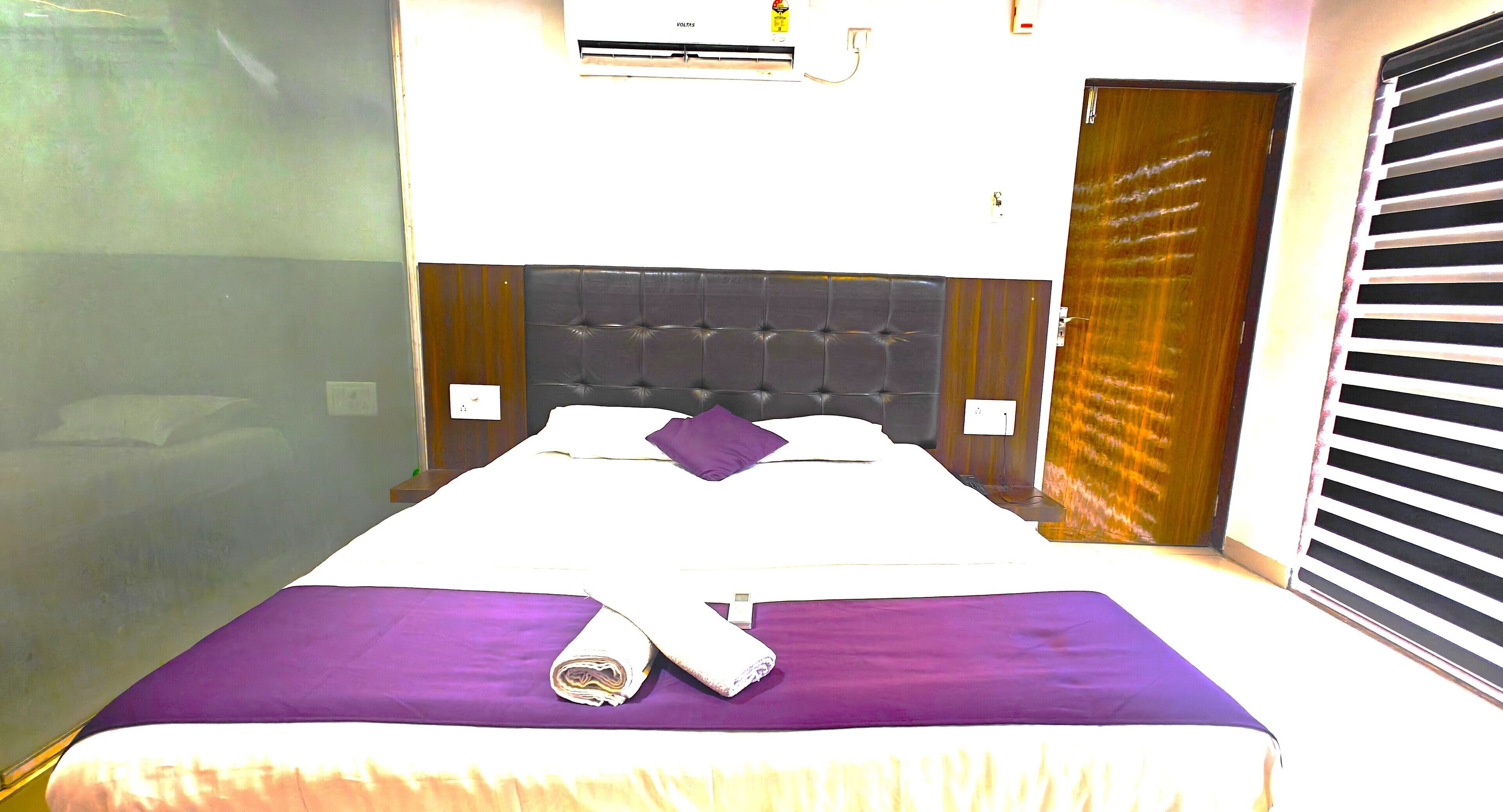 Una habitación de hotel con cama, ventana con persianas, unidad de aire acondicionado y puerta.