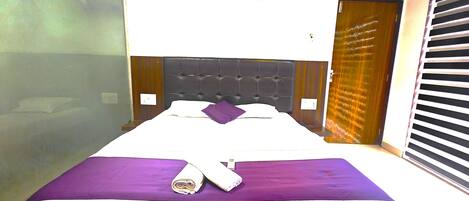 Una habitación de hotel con cama, ventana con persianas, unidad de aire acondicionado y puerta.