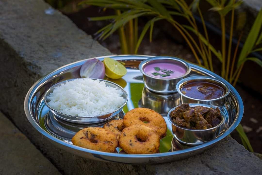 A stainless steel plate with white rice, two types of curry, a lemon wedge, and two fried snacks.
