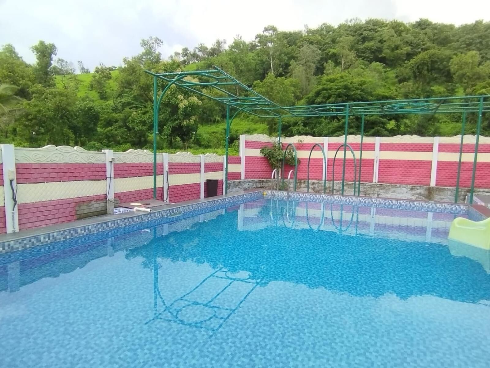 A swimming pool with a tiled deck, surrounded by a brick wall with a decorative pattern.