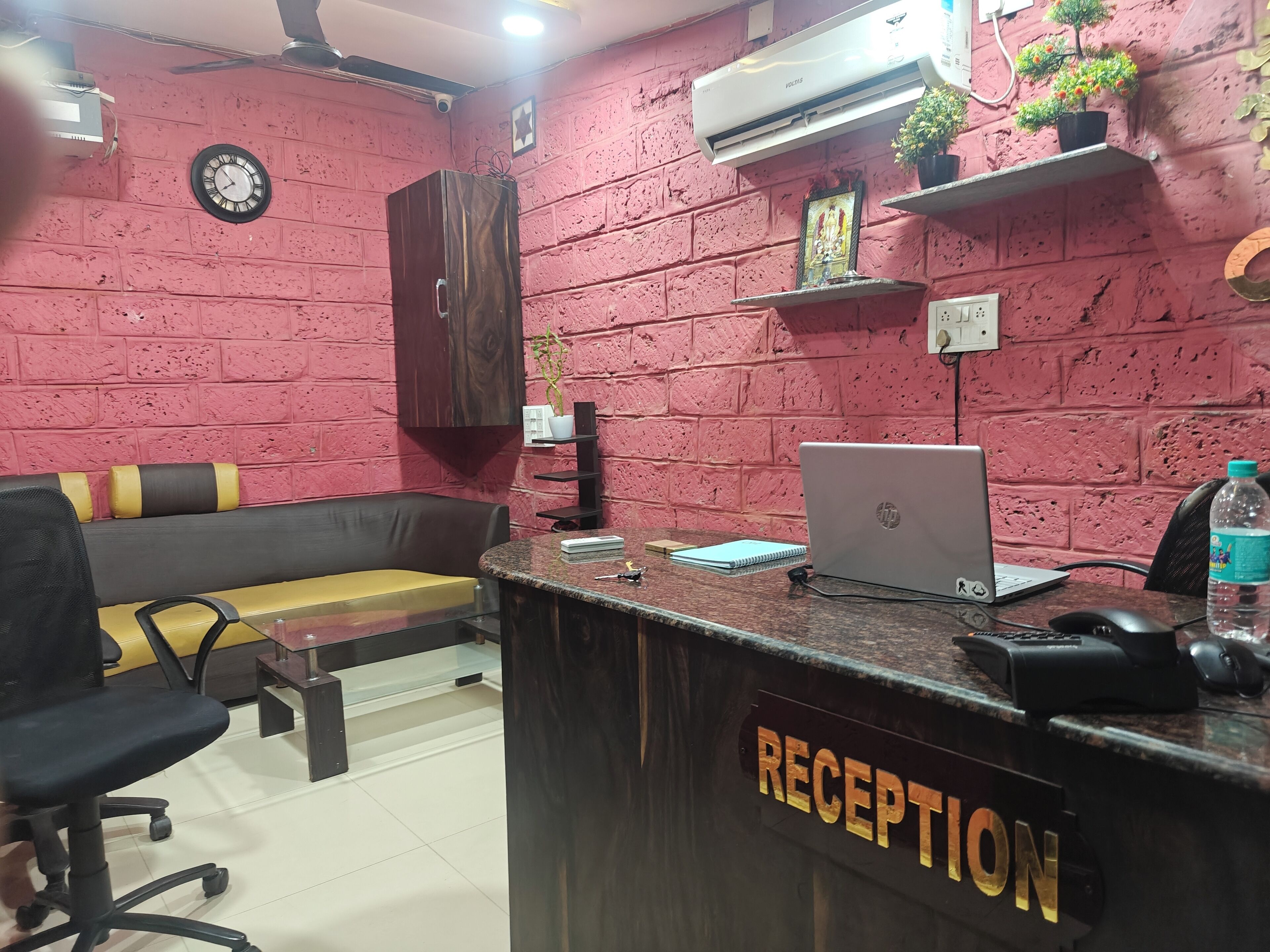 A reception area with a reception desk, a laptop, a clock, a sofa, and a plant.