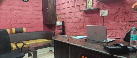 A reception area with a reception desk, a laptop, a clock, a sofa, and a plant.
