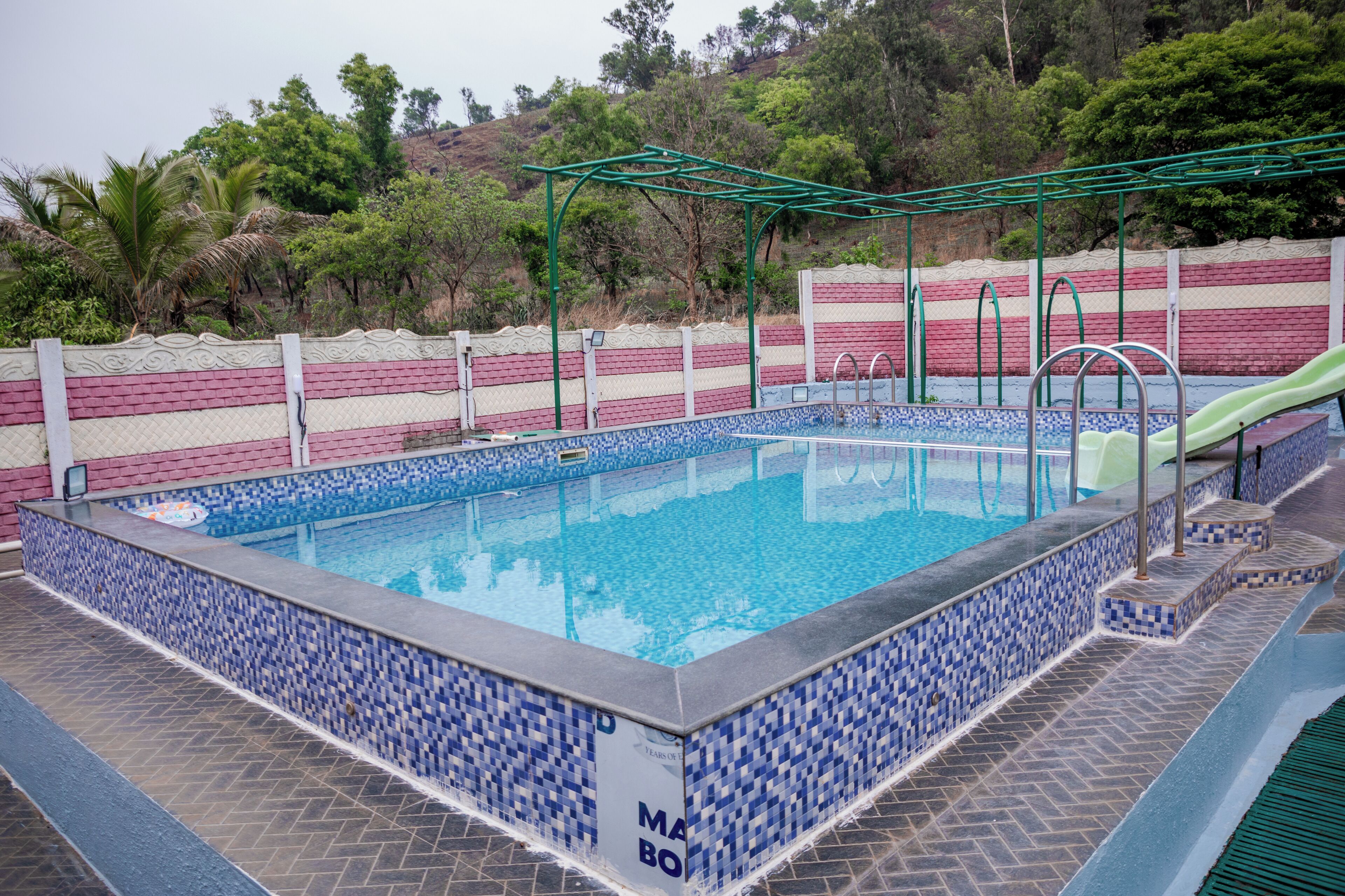 A swimming pool with a tiled border, a slide, and a green climbing structure.
