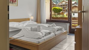 A hotel room with a wooden bed, a window with a view of buildings, and a framed picture on the wall. - View, 2 terraces & private parking - Saas-Grund (Saas-Grund)