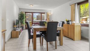 A modern dining area with a wooden table and chairs, a small kitchen area with a wooden counter, and a view of a mountain landscape through large windows. - View, 2 terraces & private parking - Saas-Grund (Saas-Grund)