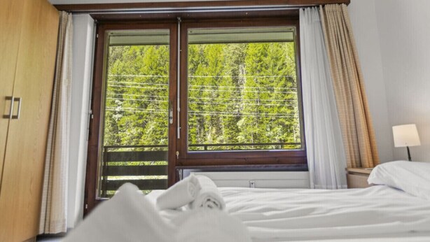A hotel room with a bed, a window with curtains, and a nightstand with a lamp. - View, 2 terraces & private parking - Saas-Grund (Saas-Grund)