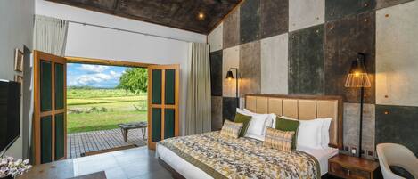 A spacious bedroom with a large bed, a wooden nightstand, a chair, and a view of the outdoors through a sliding door.