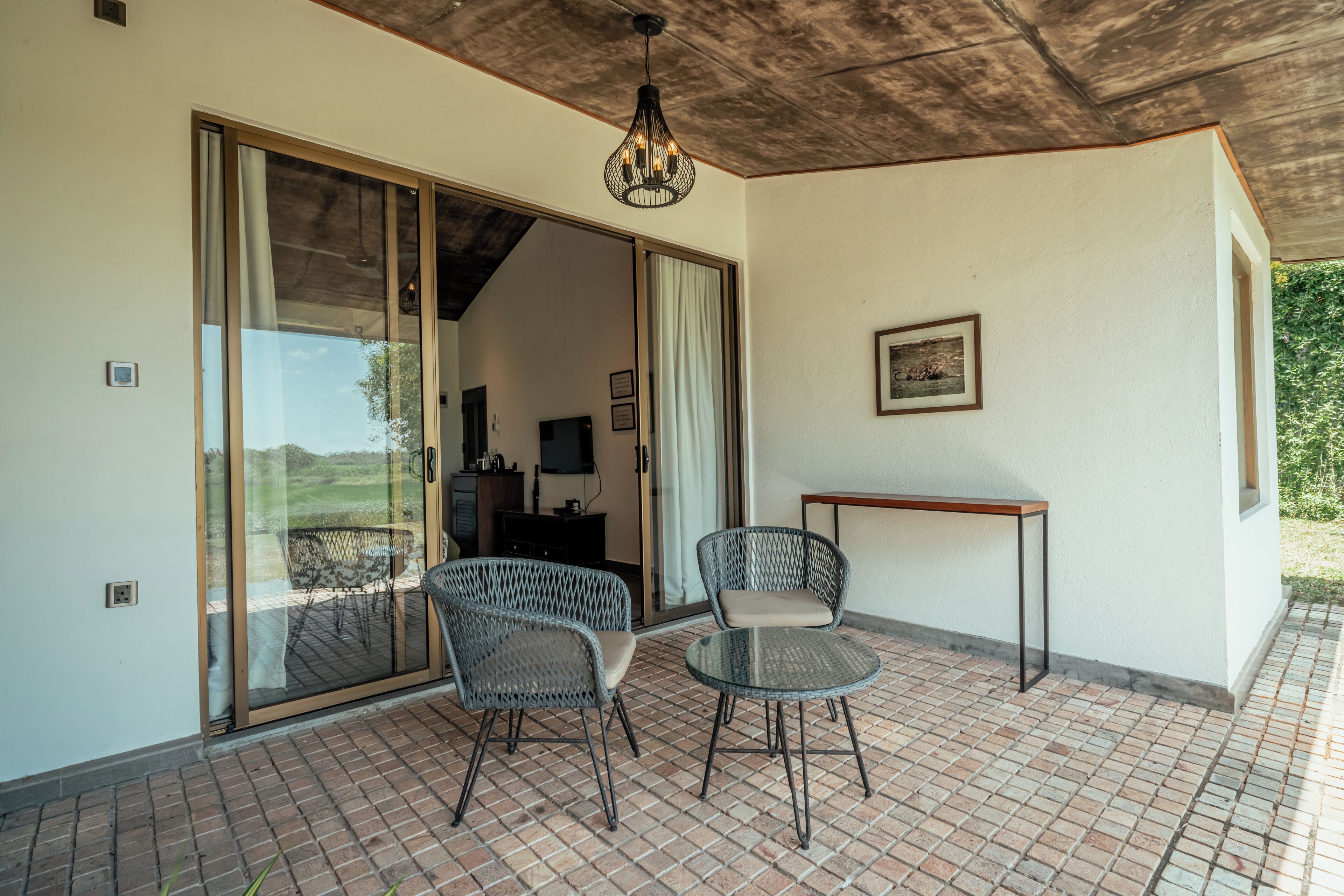 A patio with two wicker chairs and a small table, a sliding glass door leading to an interior space, and a ceiling light fixture.