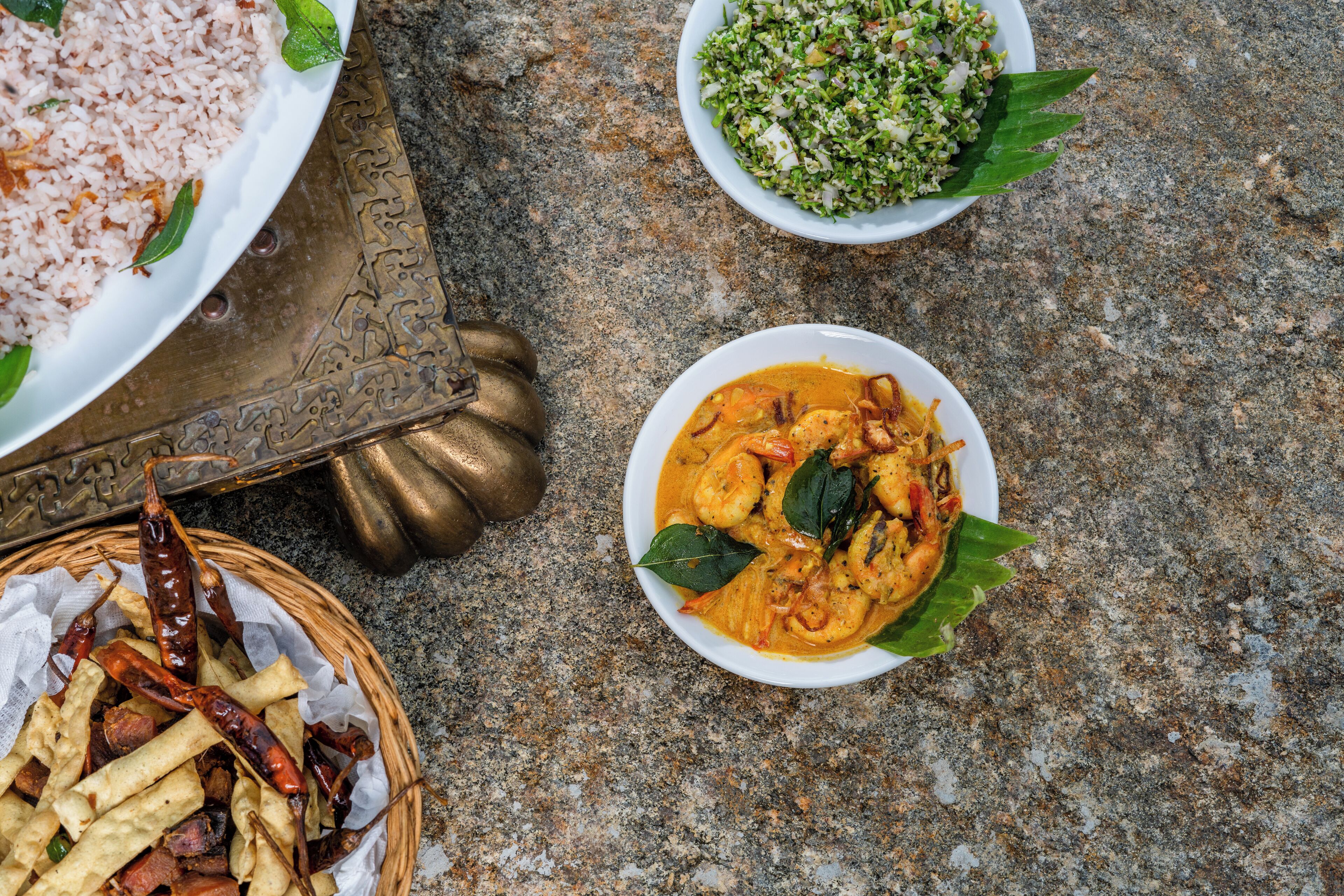 A table with a plate of rice, a bowl of curry, a bowl of salad, and a basket of fries.