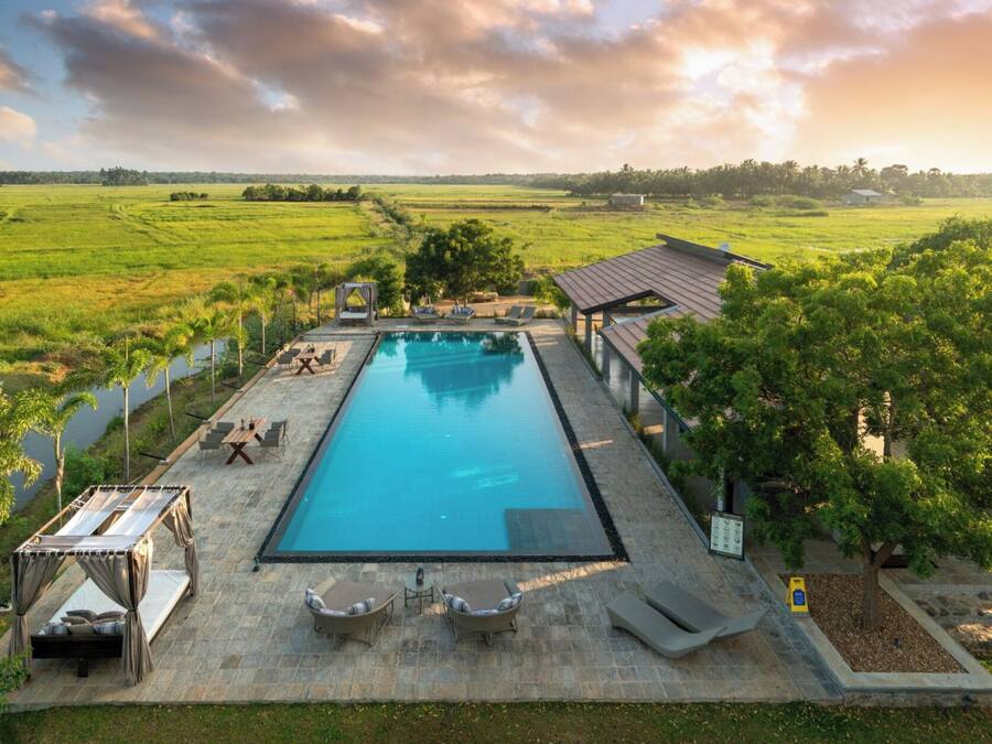 A rectangular swimming pool with a pergola and lounge chairs on one side, surrounded by a stone deck.