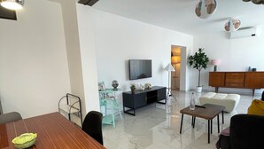 A modern living room with a wooden dining table, a sofa, and a TV. - 5 mn plages - 3 bedroom apartment - Downtown (Propriano)