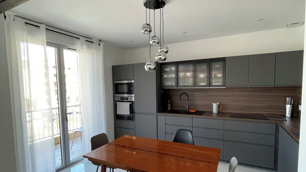 A modern kitchen with grey cabinets, a wooden dining table, and a chandelier. - 5 mn plages - 3 bedroom apartment - Downtown (Propriano)