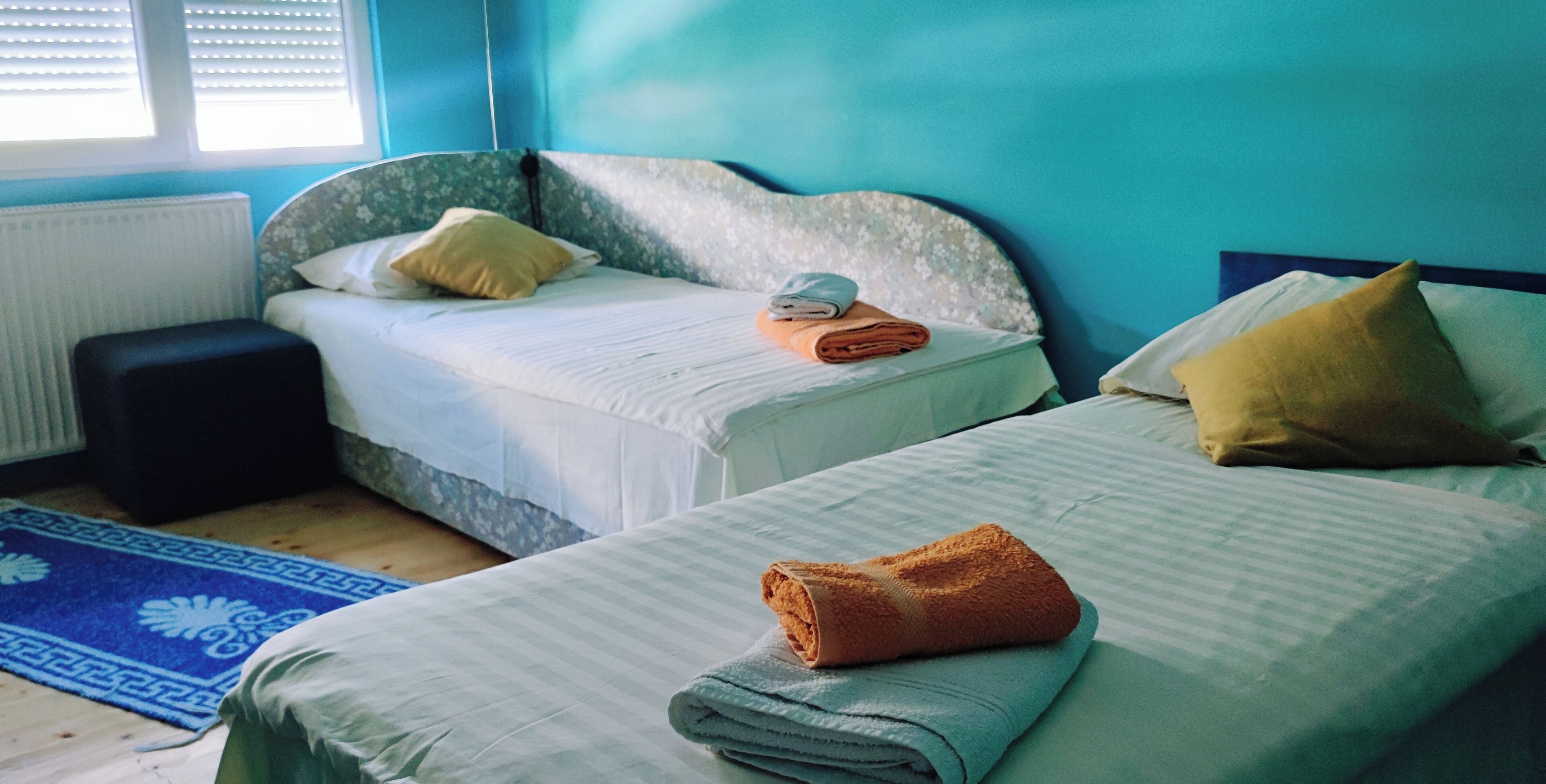 Une chambre avec deux lits, un mur bleu et une fenêtre avec des stores.