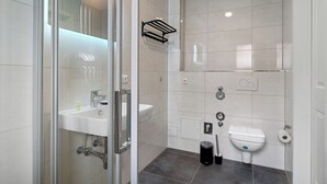 Moderni kylpyhuone, jossa on lasinen suihkuseinä, pesuallas, wc ja pyyhekoukku.
