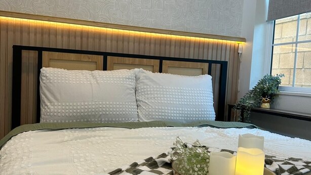 A neatly made bed with a checkered blanket, a bedside table with candles, and decorative wall art.