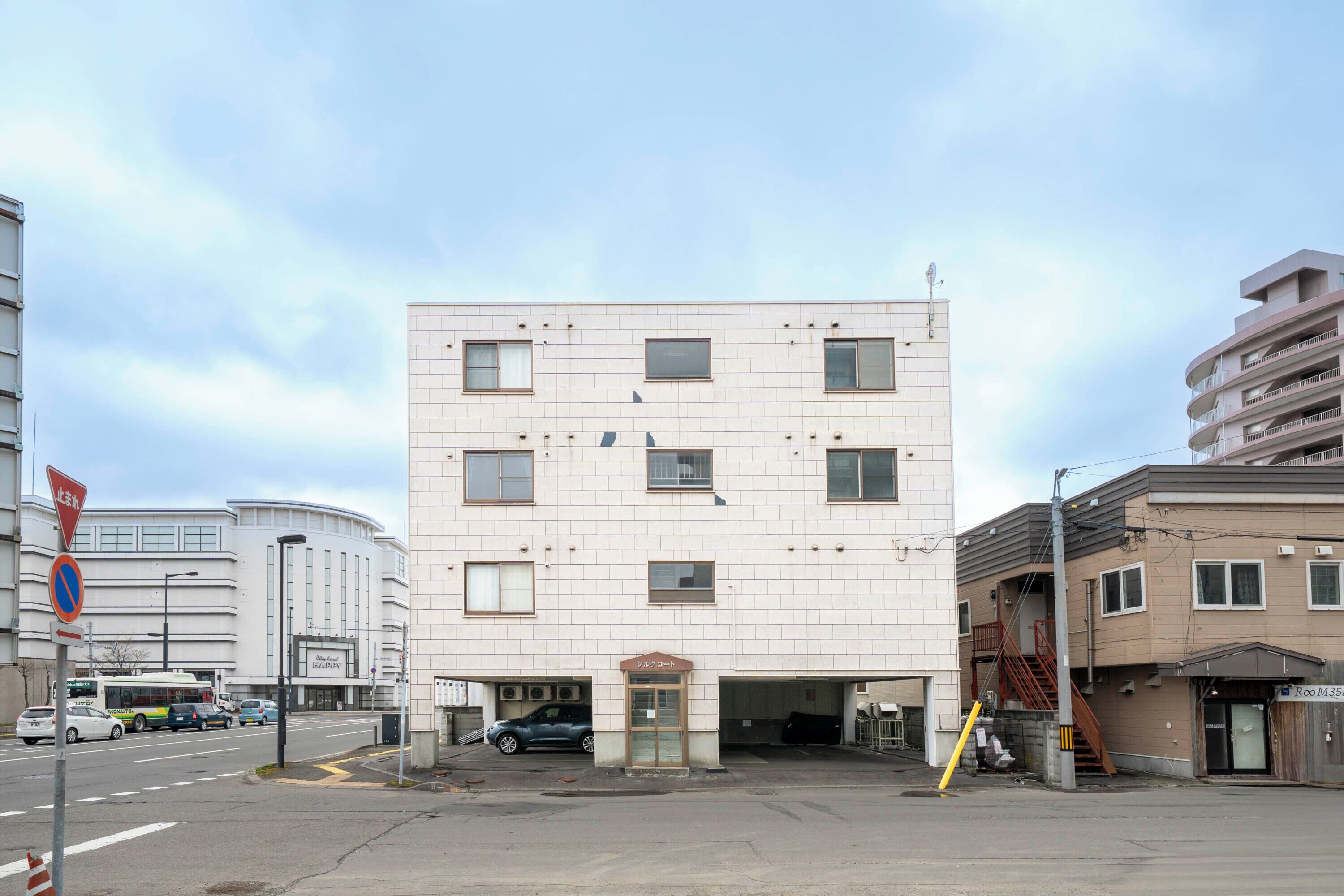 A multi-story building with a flat facade, a central entrance, and a parking area in front.