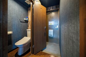 Ein kleines Badezimmer mit Toilette, Holztür und Ablage für Kosmetikartikel.