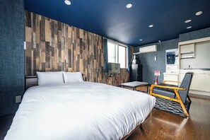 Ein modernes Hotelzimmer mit einem großen Bett, einem Schreibtisch, einem Stuhl und einer Küchenzeile.