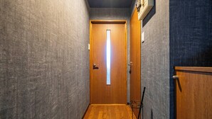 Un couloir étroit, avec une porte en bois au fond, un étagère en métal et un mur à la texture particulière.