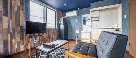 A modern living room with a flat-screen TV, a sofa, a coffee table, and a kitchen area with a microwave and refrigerator.