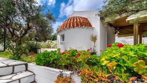 A white building with a tiled roof, surrounded by lush greenery and flowering plants.