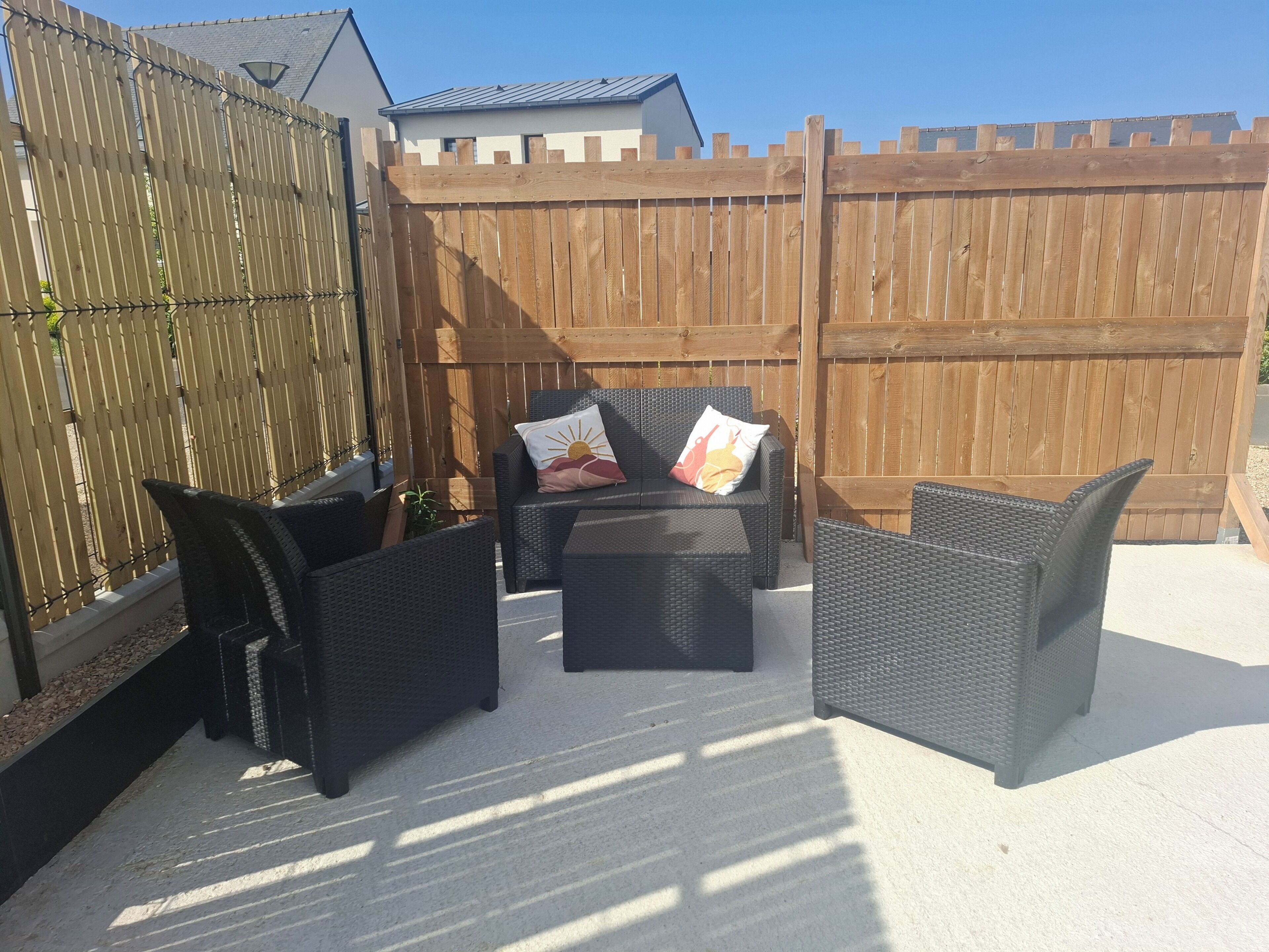 An outdoor patio area with wicker furniture and a wooden fence.