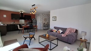 A modern living room with a sofa, coffee table, and chairs. There is a kitchen area with a dining table and chairs.