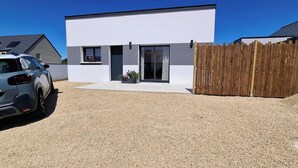 A modern two-story house with a gravel driveway, a parked car, and a wooden fence.