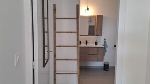A bathroom with a wooden ladder, a mirror, a sink, and a towel hanging on the wall.