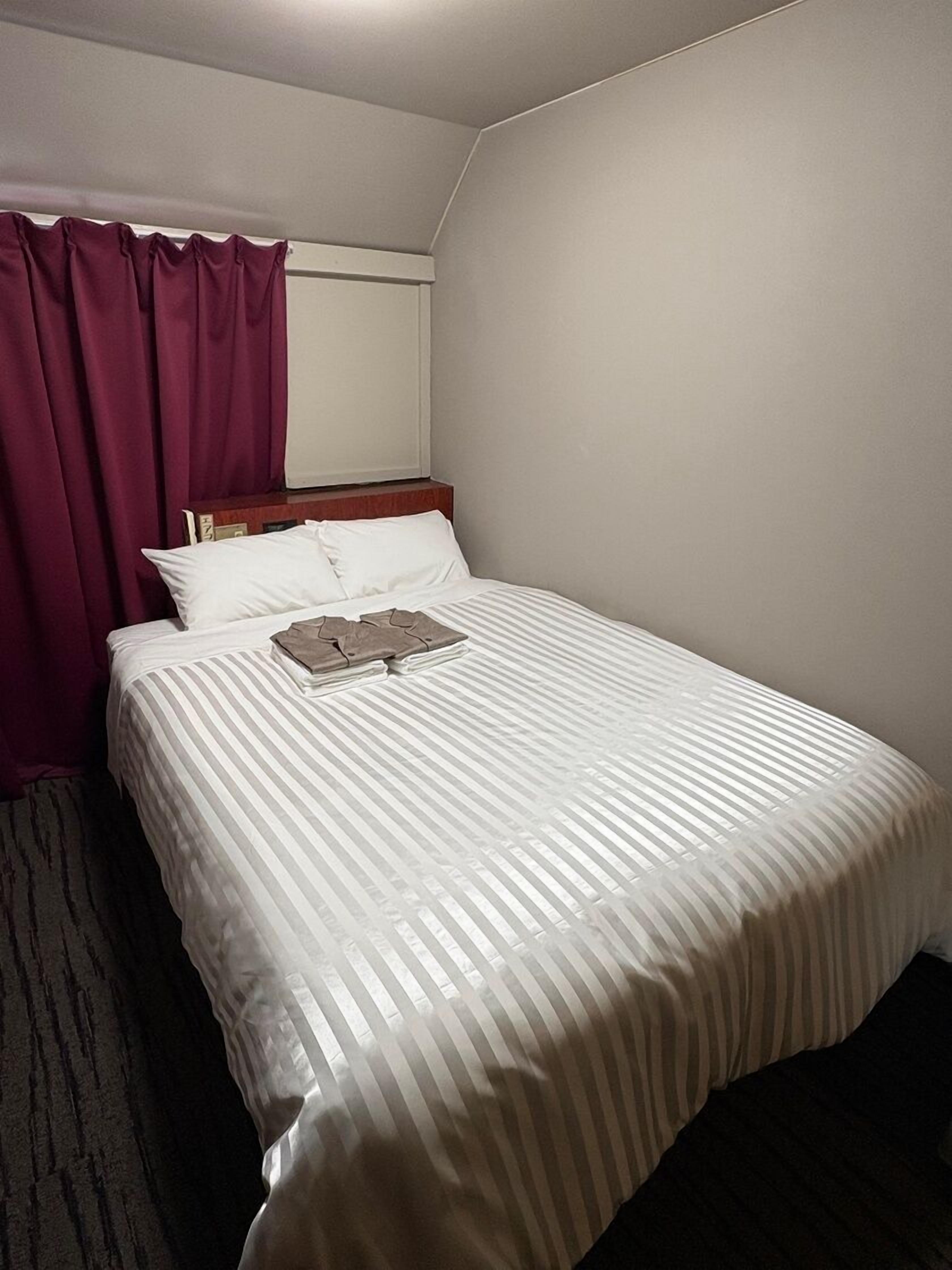 Habitación de hotel con cama, ventana con cortinas y piso alfombrado.
