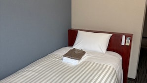 Un letto singolo con copripiumino a righe, una testiera in legno e un cuscino bianco.