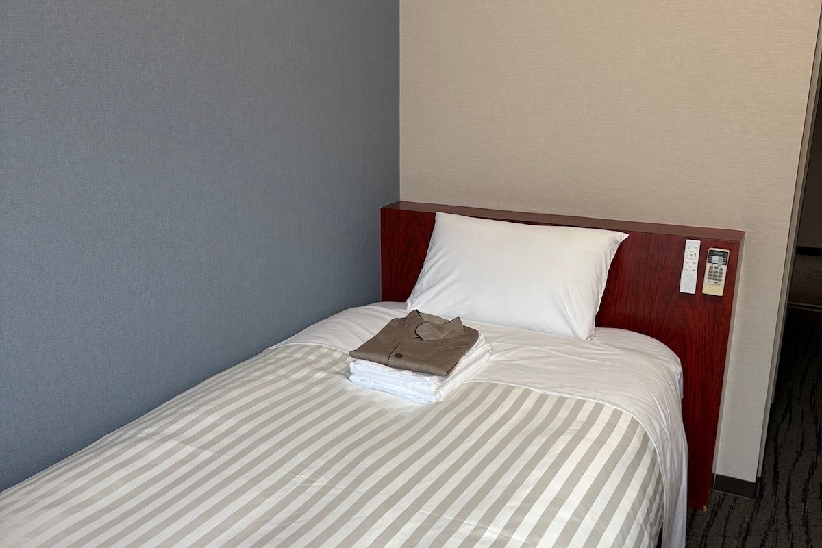 Un lit simple avec une couvre-lit à rayures, une tête de lit en bois et un oreiller blanc.