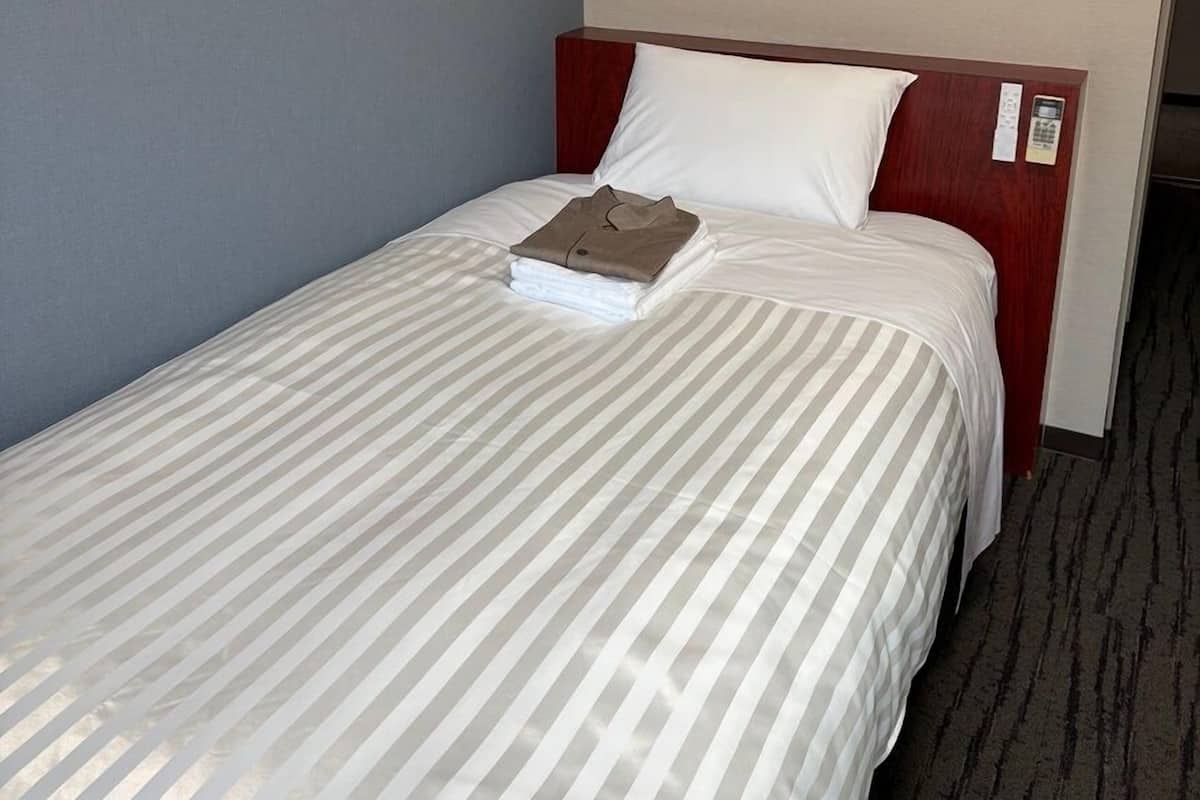 Un lit simple avec une couvre-lit à rayures, une tête de lit en bois et un oreiller blanc.