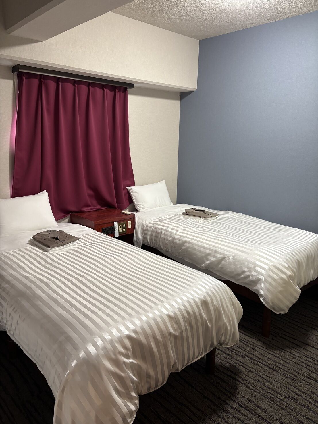 Habitación de hotel con dos camas, una mesita de noche, un teléfono y una ventana con cortinas.