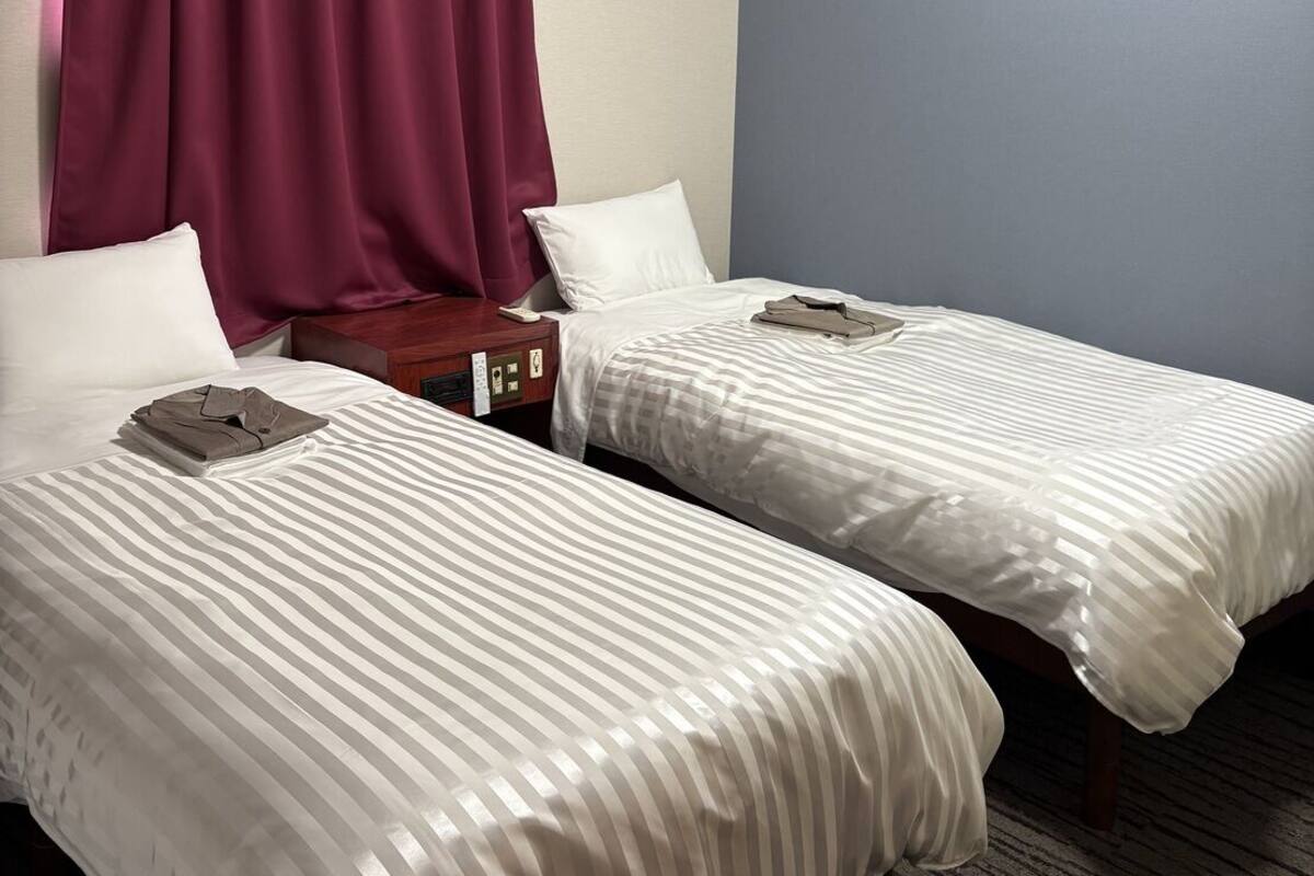 Une chambre d’hôtel avec deux lits, une table de chevet, un téléphone et une fenêtre avec des rideaux.