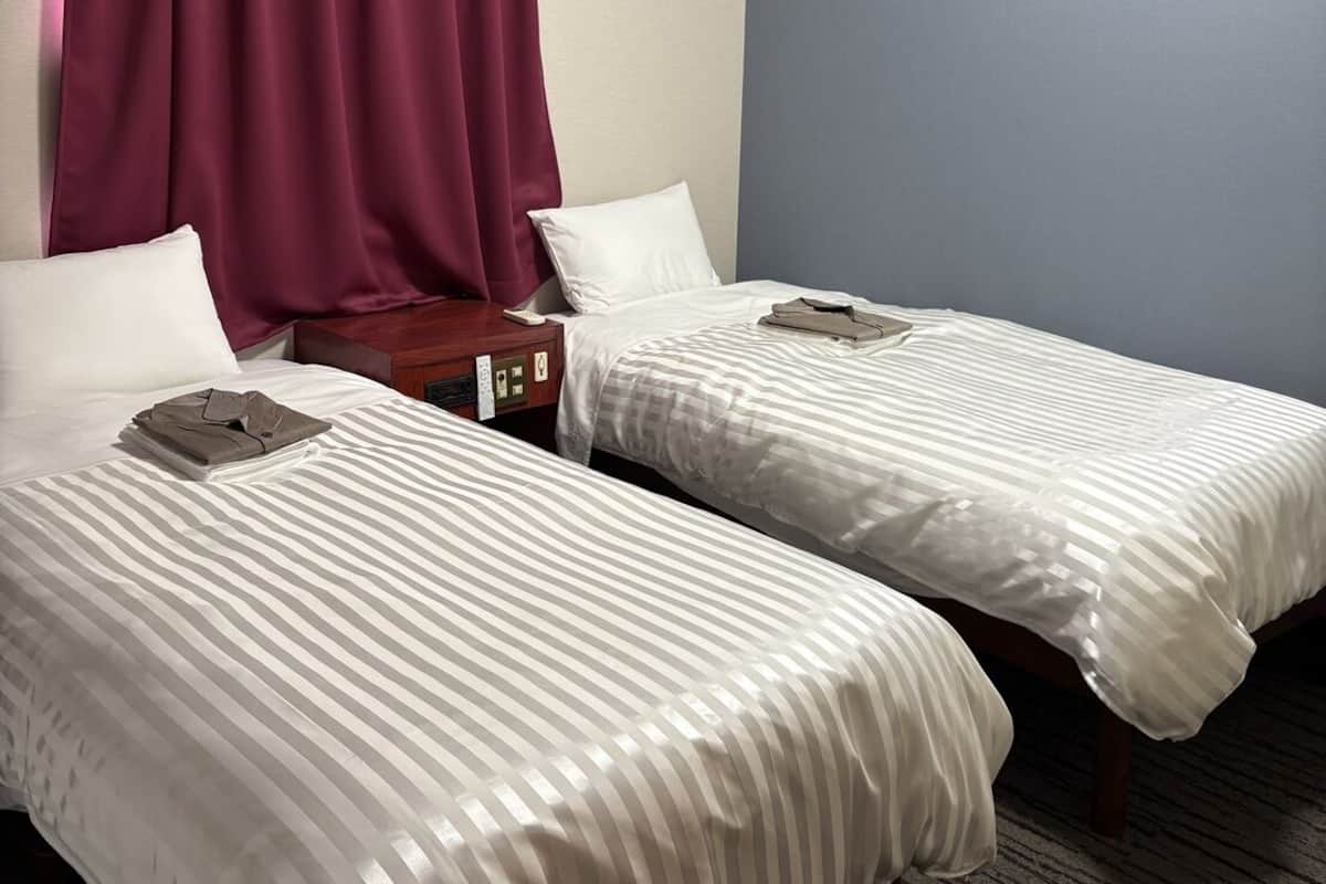 Habitación de hotel con dos camas, una mesita de noche, un teléfono y una ventana con cortinas.