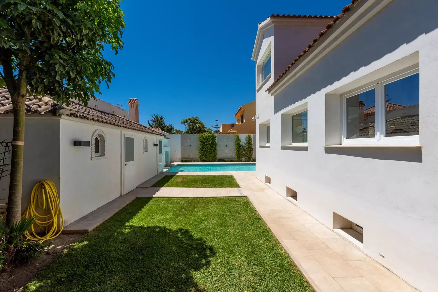 A modern house with a swimming pool, a well-maintained lawn, and a clear blue sky.