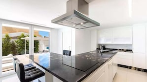 Una cocina moderna con una isla grande, armarios blancos y vistas a un balcón con mobiliario de exterior.