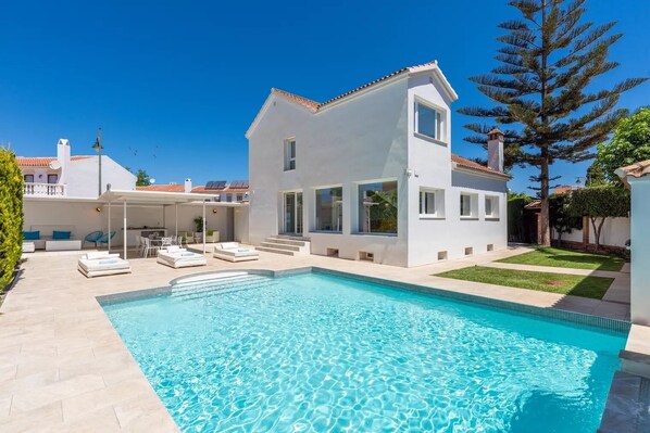 A modern two-story house with a swimming pool, a covered patio, and a well-maintained lawn.