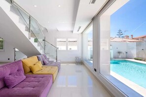 A modern interior with a sofa set, a staircase, and a view of a swimming pool.